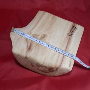 May include: A light-coloured wooden cutting board with a natural edge. A measuring tape is laid across the board, showing a length of approximately 56 cm. The word "Wood" is printed on the board.