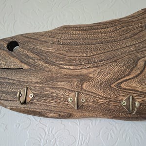 May include: A rustic wooden wall-mounted key holder with three metal hooks. The wood has a dark brown finish with visible grain patterns. The hooks are diamond-shaped with a bronze finish, perfect for organizing keys or small items.