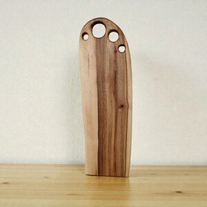 Pode incluir: Uma t&aacute;bua de corte de madeira alta e vertical com um padr&atilde;o de gr&atilde;o natural em tons de castanho claro e escuro. A extremidade superior &eacute; arredondada e apresenta quatro aberturas circulares de tamanhos variados numa fila horizontal.