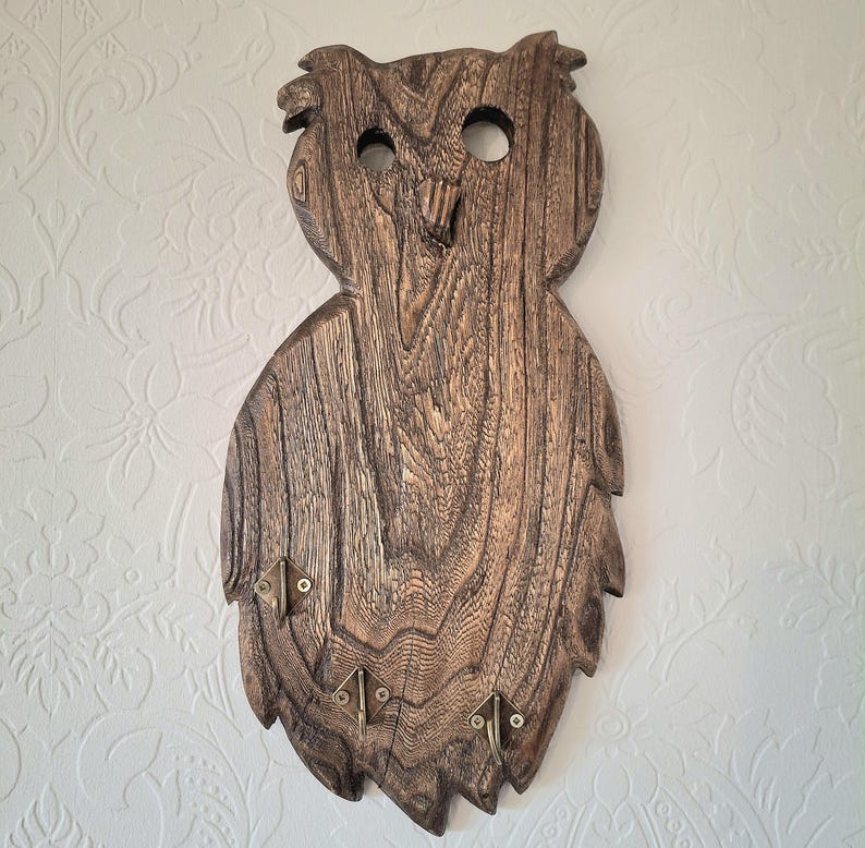 May include: Wooden owl-shaped key holder with a natural wood grain finish. The key holder has three brass-colored hooks at the bottom and two eye holes. The owl's head has a textured appearance, and the overall design is rustic.