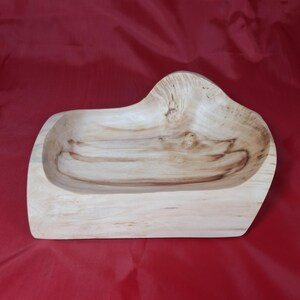 May include: A handcrafted wooden bowl with an unusual, organic form. The bowl is made from light-coloured wood with visible grain patterns and a smooth, polished finish. The bowl's dimensions are approximately 30 cm long, 20 cm wide, and 8 cm deep.