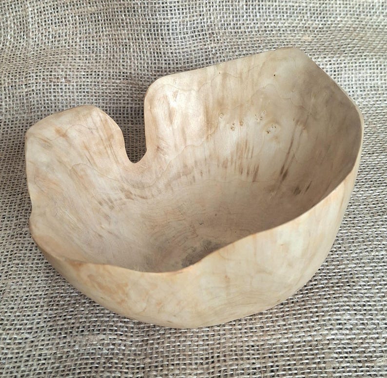 Op de afbeelding: Een handgemaakte houten kom met een lichte kleur en een organische vorm. De kom heeft een opvallende uitsparing en toont natuurlijke houtnerfpatronen. Geschikt voor serveren of decoratie. De diameter is ongeveer 25 cm.