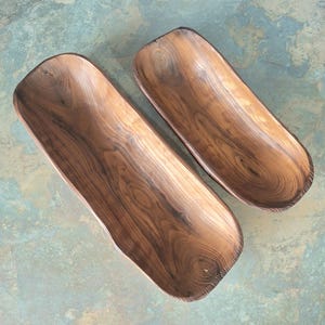 May include: Two wooden, rectangular bowls with a natural wood grain pattern. The bowls are a warm brown color and have a smooth, polished finish. The bowls are empty and appear to be handmade.