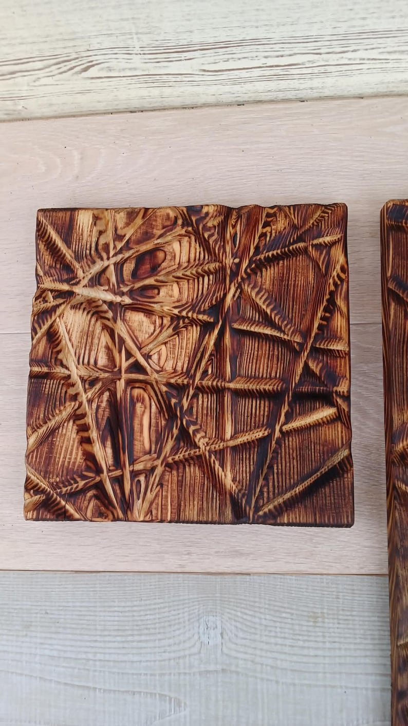 May include: Two square wooden panels with a geometric, textured design. The wood has a warm, brown tone with darker, burnt accents in the carved areas. The design features intersecting lines and shapes.