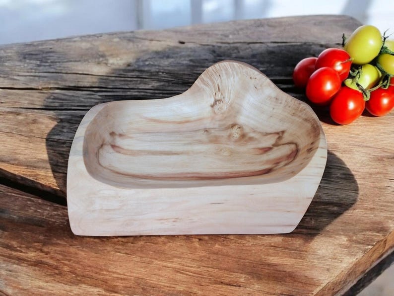 May include: A wooden bowl with a natural finish and an organic shape. The bowl is displayed on a wooden surface. Red and yellow tomatoes are in the background. The bowl's dimensions are in centimetres.