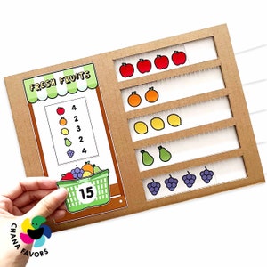 May include: A cardboard learning game for kids with a fruit theme. The game has a stand with a sign that says "Fresh Fruits" and a basket of fruit with a number 15 on it. There are also several rows of fruit with numbers next to them.
