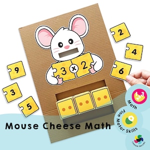 Op de afbeelding: Een kartonnen spel voor kinderen met een cartoonmuis die twee stukjes kaas vasthoudt met de nummers 3 en 2 erop. Het spel bevat een gleuf om genummerde puzzelstukjes in te laten vallen en een rij kaasblokken met stippen die nummers voorstellen. Het spel heet "Mouse Cheese Math" en bevat de woorden "Math", "Motor Skills" en "CHANA FAVORS".