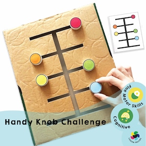 May include: A handmade cardboard toy labeled "Handy Knob Challenge" with colorful knobs. The game features a maze-like design with slots for the knobs to slide through. The image also includes a reference card with a matching pattern.