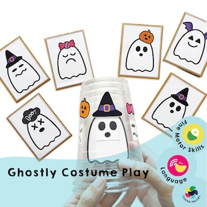 May include: A set of six ghost-themed cards with different costumes and expressions. The cards are printed on white cardstock with black outlines and colorful details. The cards are arranged around a clear plastic cup with a ghost sticker on it. The cup is being held by a hand. The text "Boo!" is on one of the cards. The text "Ghostly Costume Play" is at the bottom of the image. The text "Fine Motor Skills" and "Language" are on the right side of the image.