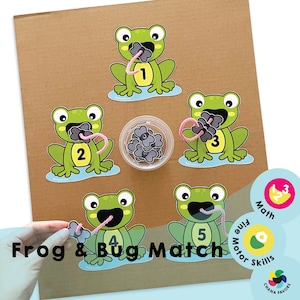 May include: A frog and bug matching game for children. Five green frogs with pink tongues are holding different numbers of black bugs. The game includes a container of black bugs and a set of number cards.