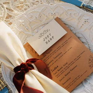 Może przedstawiać: Brązowe menu z papieru z białą kartką na górze, na której widnieje napis "JOEY HANF". Menu zawiera następujące pozycje: Chicken Pignoli, Vegetable Tortellini, Dodatki, Sałatka z jesiennego rynku, Ziemniaki puree z czosnkiem i Brokuły.
