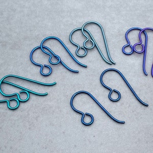 May include: A set of eight blue and purple titanium earring hooks. The hooks are made of metal and have a smooth, polished finish.