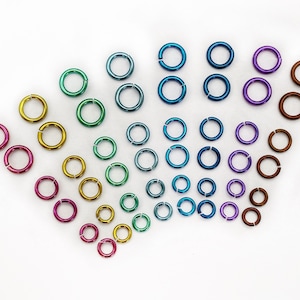 May include: Assortment of colourful metal jump rings in various sizes, arranged in a rainbow pattern. The jump rings are made of metal and have a shiny finish.