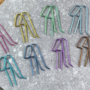 May include: A set of ten pairs of earrings in various colors, including purple, blue, green, gold, and brown. Each pair is made of a single piece of wire bent into a unique shape.