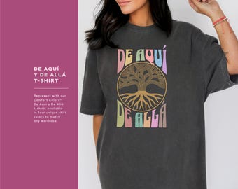 May include: A black t-shirt with a colorful graphic design featuring a tree with roots and the text "DE AQUÍ DE ALLÁ".