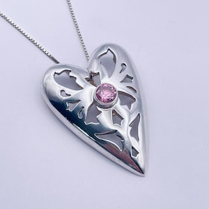 May include: A silver heart-shaped pendant necklace with a delicate filigree design and a pink gemstone in the centre.