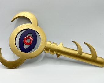 May include: A golden key-shaped object with a circular design at the top, featuring a blue and red center. The handle has a series of spikes and curved edges. The key is likely a decorative item or prop.