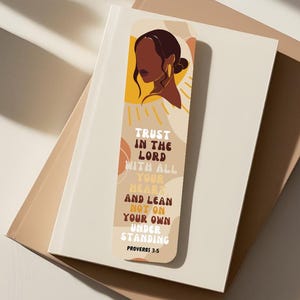 Può includere: Un segnalibro beige con un design astratto colorato che presenta una donna con la pelle marrone e uno sfondo giallo. Il segnalibro include il testo "TRUST IN THE LORD WITH ALL YOUR HEART AND LEAN NOT ON YOUR OWN UNDERSTANDING PROVERBS 3.5".