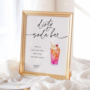 May include: A framed sign with gold trim, featuring the words "dirty soda bar" in elegant script. Below, instructions for making a soda are listed, accompanied by a watercolor illustration of a soda with whipped cream and a cherry. The word "enjoy!" is at the bottom.