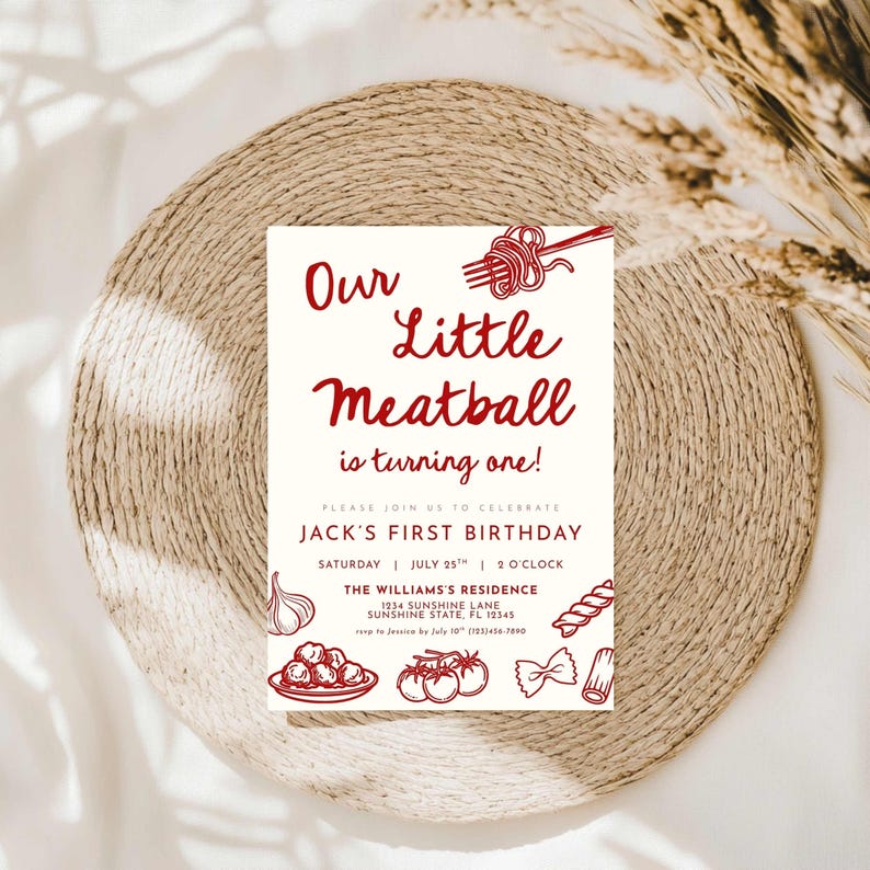 Może przedstawiać: Kremowe zaproszenie z czerwonym tekstem i ilustracjami na pierwsze urodziny. Tekst brzmi "Our Little Meatball is turning one!" ze szczeg&oacute;łami przyjęcia. Zaproszenie leży na plecionym podkładce, o średnicy około 30 cm.