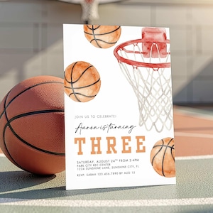 Puede incluir: Una invitación de cumpleaños con temática de baloncesto con balones de baloncesto y una canasta en acuarela. La invitación dice "Aaron is turning THREE" con detalles del evento. Una pelota de baloncesto real descansa al lado.