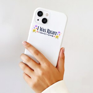 May include: White phone case with the text "I WAS RIGHT I listened to my body" in navy blue, decorated with colorful floral accents. The phone case has a dual-lens camera.