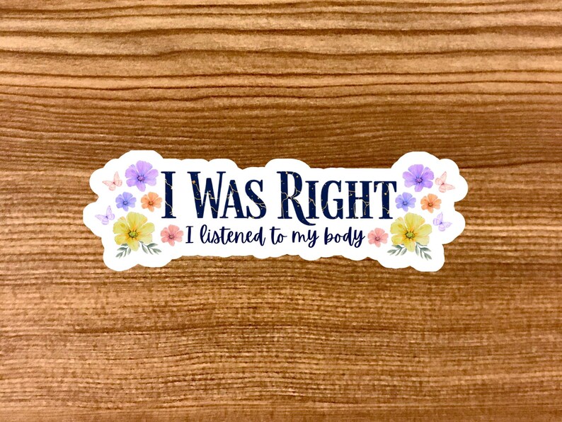 May include: A white sticker with the text "I WAS RIGHT" in navy blue, with "I listened to my body" below. The sticker is decorated with colorful flowers and butterflies, set against a wooden background.
