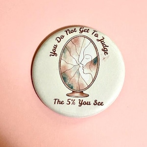 Peut inclure: Un badge rond à épingle sur fond blanc avec une illustration marron d'un miroir ovale brisé et une silhouette de profil. Le texte, You Do Not Get To Judge The 5% You See, est inscrit en lettres marron autour du motif central.