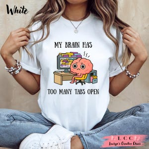 K&ouml;nnte beinhalten: Wei&szlig;es T-Shirt mit dem Text "MY BRAIN HAS TOO MANY TABS OPEN". Die Grafik zeigt ein Cartoon-Gehirn, das an einem Computer mit vielen ge&ouml;ffneten Tabs sitzt. Das Gehirn hat einen besorgten Gesichtsausdruck.