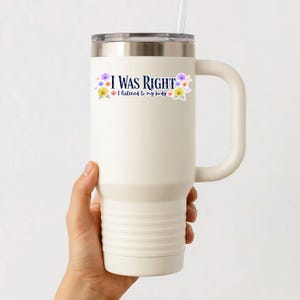 May include: A white travel mug with a silver lid and a handle. The mug has the text "I WAS RIGHT" with the phrase "I listened to my body" below it, and is decorated with floral accents. A straw is inserted into the lid.
