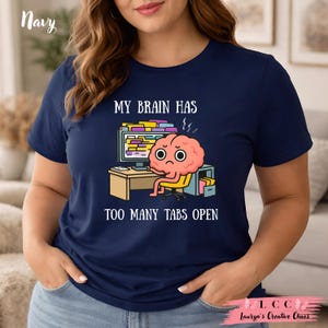 K&ouml;nnte beinhalten: Marineblaues T-Shirt mit dem Text "MY BRAIN HAS TOO MANY TABS OPEN" und einer Cartoon-Gehirnfigur, die an einem Schreibtisch mit einem Computer sitzt. Das Gehirn hat einen gestressten Ausdruck.
