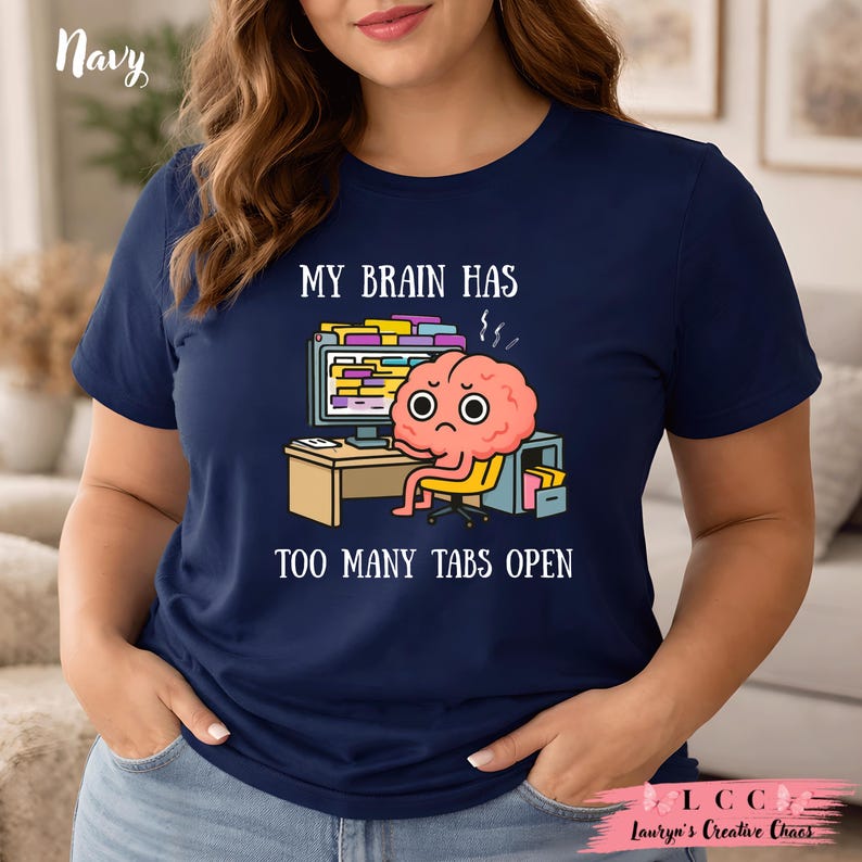 K&ouml;nnte beinhalten: Marineblaues T-Shirt mit dem Text "MY BRAIN HAS TOO MANY TABS OPEN" und einer Cartoon-Gehirnfigur, die an einem Schreibtisch mit einem Computer sitzt. Das Gehirn hat einen gestressten Ausdruck.