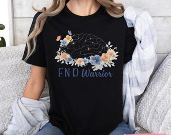 May include: Black t-shirt featuring a floral brain design with the text "FND Warrior". The design includes blue, orange, and white flowers. The shirt is a crew neck and has short sleeves.