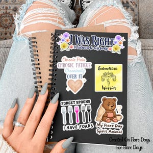 May include: A black spiral-bound notebook with various stickers. Stickers include text that reads "I was right, I listened to my body", "Chronic Pain, Chronic Fatigue, Chronically Over It", "Forget Spoons, I Have Forks", and "My Flare Day Spirit Animal".