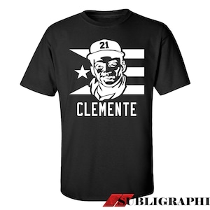 Puede incluir: Camiseta negra con un diseño blanco de un jugador de béisbol con una gorra con el número 21. El diseño incluye la bandera de Puerto Rico y el nombre "CLEMENTE".