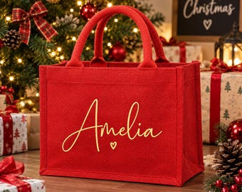 Könnte beinhalten: Eine rechteckige Tragetasche aus rotem Jute-Stoff mit zwei Tragegriffen. Auf der Vorderseite der Tasche ist der Name Amelia in einer goldenen Schreibschrift aufgedruckt, ergänzt durch ein kleines goldenes Herzsymbol unter dem Namen.