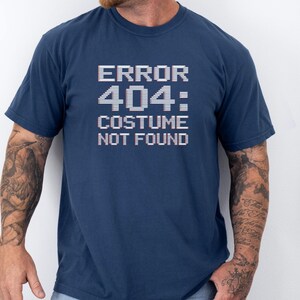 May include: A navy blue t-shirt with the text "ERROR 404: COSTUME NOT FOUND" in white pixelated font. The short-sleeved shirt is made of a soft material. The design is centered on the chest.