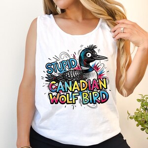 以下が含まれることがあります： 白いタンクトップ。漫画のイラストで、アビと「STUPID CANADIAN WOLF BIRD」の文字が描かれています。鳥は黒い頭、青いアクセント、白黒の体をしており、カラフルな文字が周りにあります。