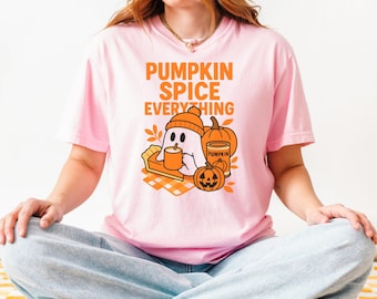 May include: Pink t-shirt with the text "PUMPKIN SPICE EVERYTHING" in orange. The graphic features a ghost wearing a beanie, holding a mug, with a pumpkin pie, pumpkins, and fall leaves. The shirt is a casual, fall-themed design.
