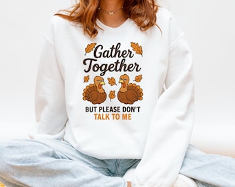 Può includere: Felpa bianca con la scritta "Gather Together" e "But Please Don't Talk To Me". Il design presenta due tacchini dei cartoni animati e foglie autunnali nei toni del marrone e dell'arancione. Un top casual e confortevole.