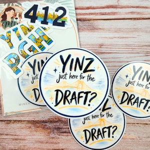 May include: A collection of stickers featuring the city name "YINZ" with the text "just here for the DRAFT?" and a bridge illustration. Other stickers include the number "412" and the city name "YINZBURGH".