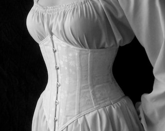 May include: A white corset with a satin finish and a row of silver buttons down the front. The corset is worn over a white blouse with a gathered neckline.