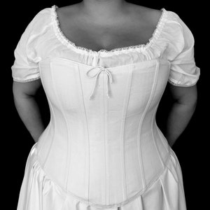 May include: A white corset with a lace trim and a bow at the centre. The corset is made of a smooth, silky fabric and has a fitted silhouette.