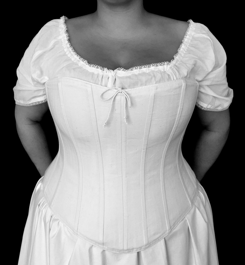 May include: A white corset with a lace trim and a bow at the centre. The corset is made of a smooth, silky fabric and has a fitted silhouette.