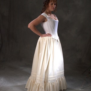 May include: A white cotton corset with a low neckline and a gathered skirt. The corset has a fitted bodice and a full skirt with ruffles at the hem.