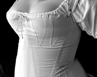 May include: A white cotton corset with a lace-up front and a ruffled hem. The corset has a V-shaped neckline and is designed to cinch the waist.