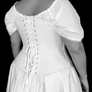 May include: A white corset with a lace-trimmed bodice and a long, flowing skirt. The corset has a lace-up back with white ribbon ties.