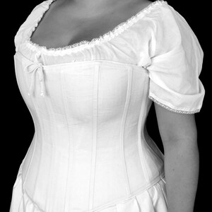 May include: A white cotton corset with a lace trim and a gathered neckline. The corset has a boned structure and a long, flowing skirt.
