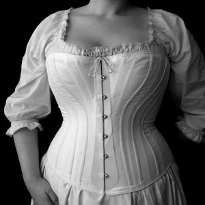 May include: A white corset with a lace trim and a row of silver buttons down the front.