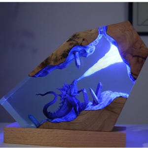 May include: A unique, handcrafted resin sculpture featuring a blue dragon breathing a white beam. The sculpture is encased in clear resin with wooden accents and sits on a wooden base. The dragon is surrounded by blue crystals.